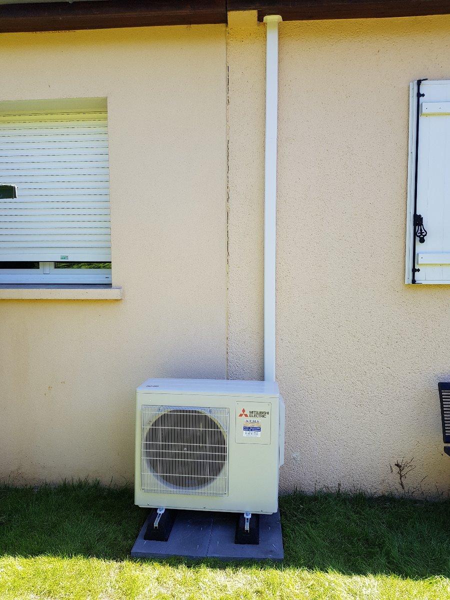 Unité extérieure d'une pompe à chaleur avec cache-cables verticale montant le long du mur blanc derrière