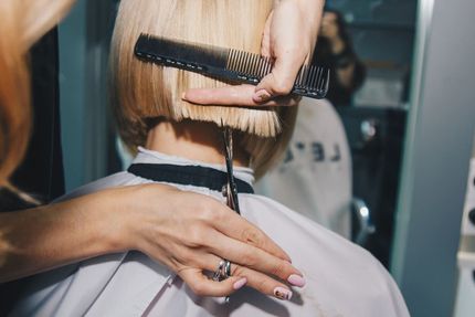 Peluquera cortando cabello rubio corto con tijeras y peine en un salón de belleza.