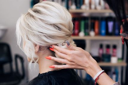 Arreglando a mano el cabello rubio corto en una peluquería, con estantes de productos difuminados al fondo.
