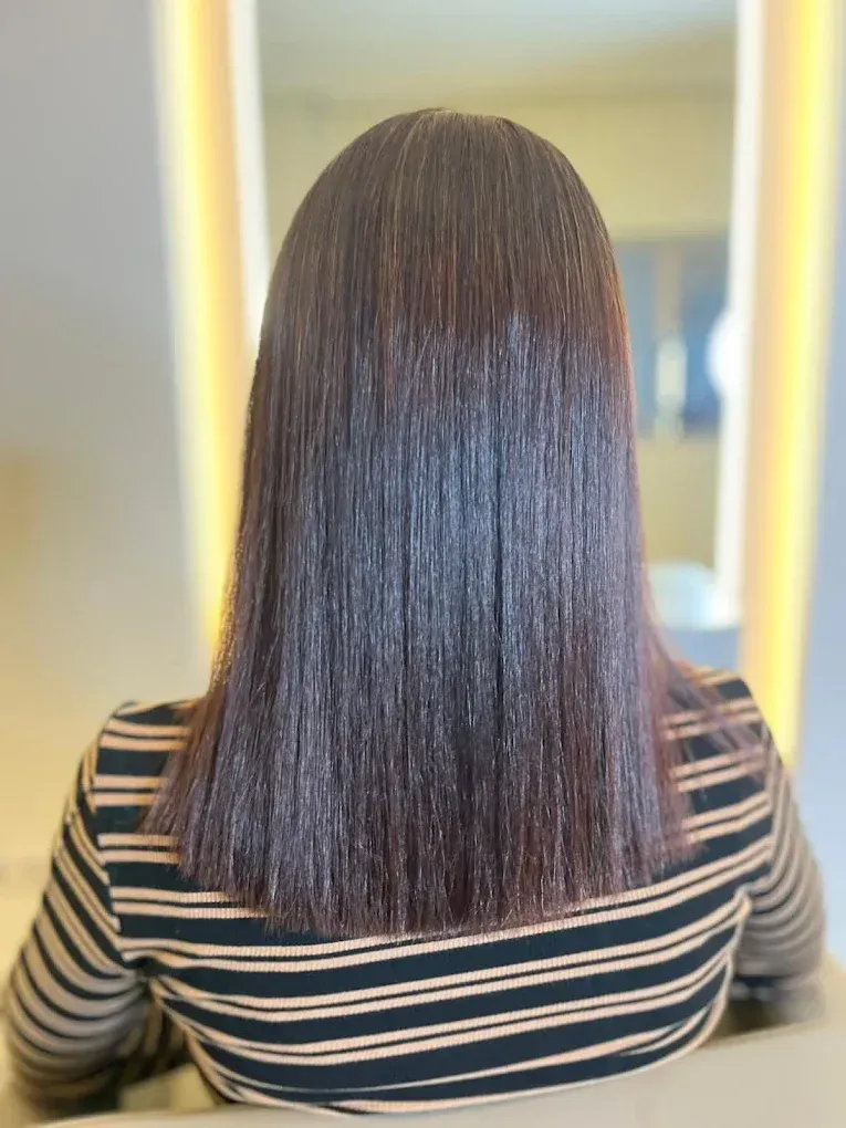 Persona con cabello oscuro y encrespado que usa una capa de salón, vista desde atrás en un espacio muy iluminado.