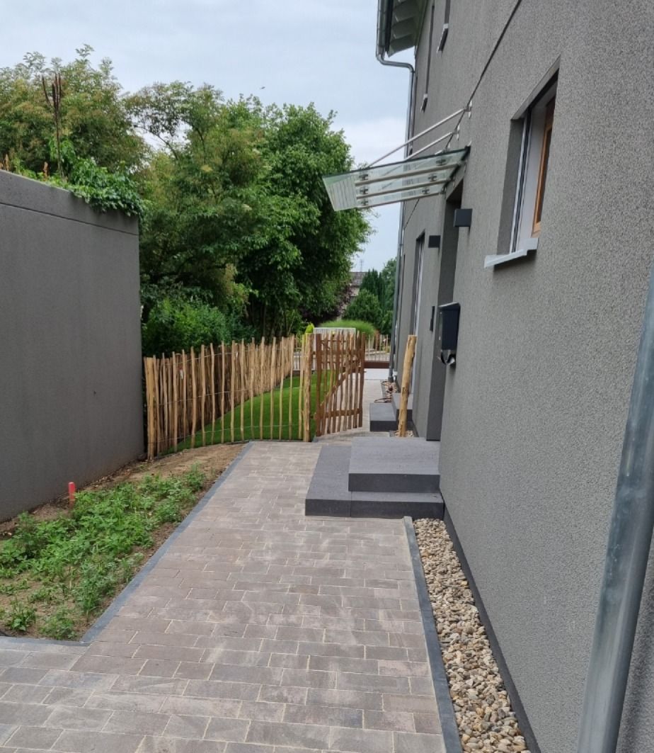 Ein graues Haus mit gepflastertem Gehweg, Holzzaun und Glasvordach.