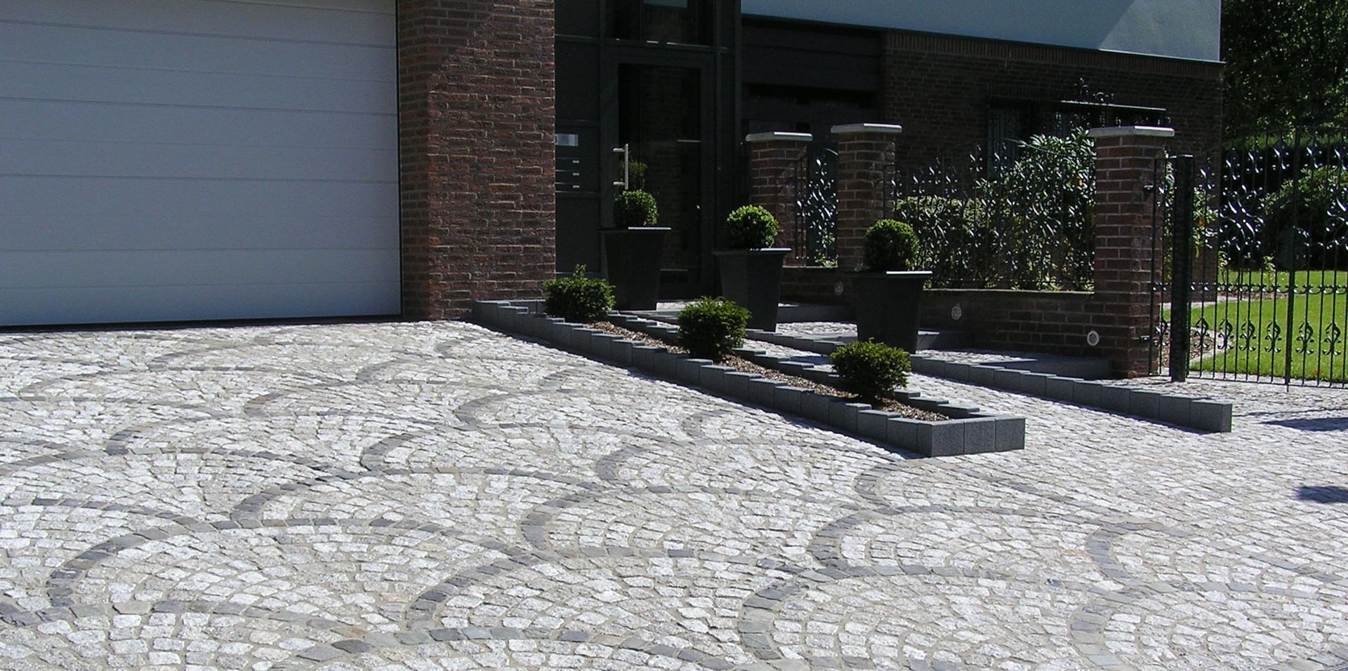 Eine mit Kopfsteinpflaster verzierte Auffahrt führt zu einem modernen Haus mit ansprechender Gartengestaltung.