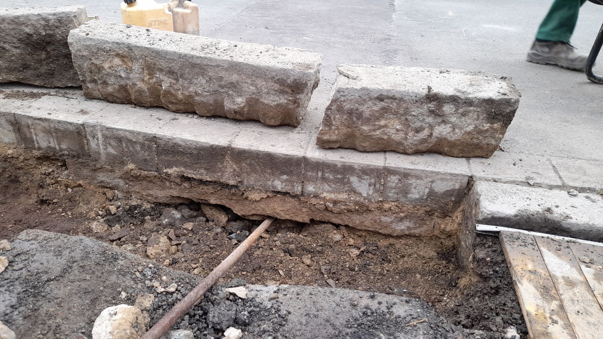 Baustelle, auf der Pflastersteine ​​entfernt wurden, wodurch unterirdische Erde und eine Metallstange sichtbar werden.