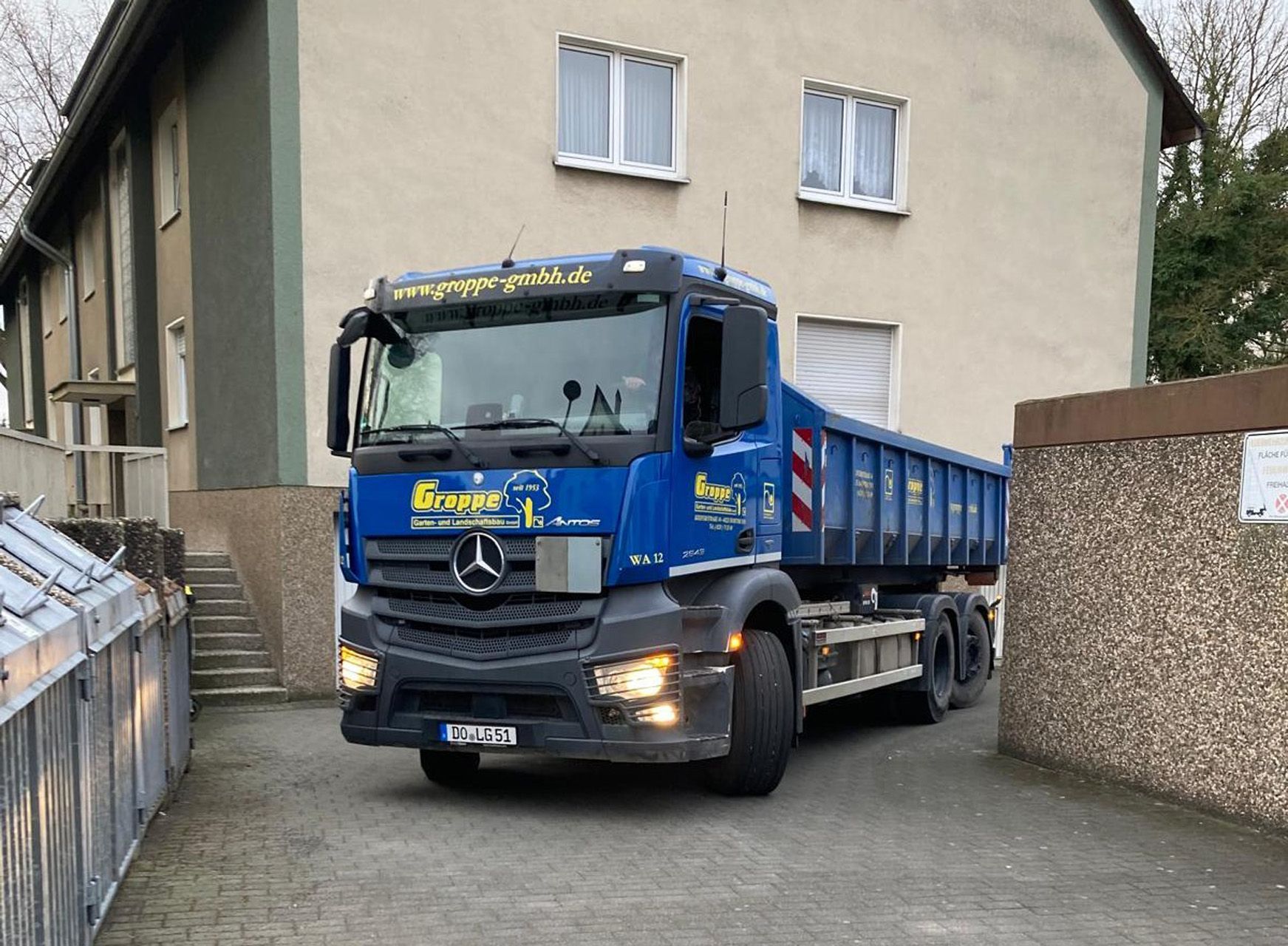 Ein blauer Mercedes-Kipper parkt vor einem Gebäude mit hellgrauer Außenfassade.