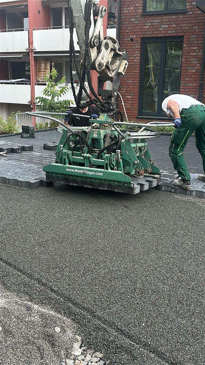 Grüne Asphaltwalze und Arbeiter verdichten frisch asphaltierte Fahrbahn.