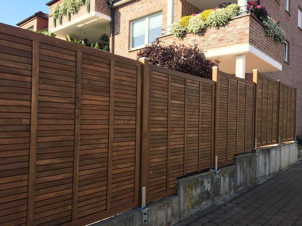 Brauner Sichtschutzzaun aus Holz entlang eines Backsteingebäudes mit Blumenkästen.