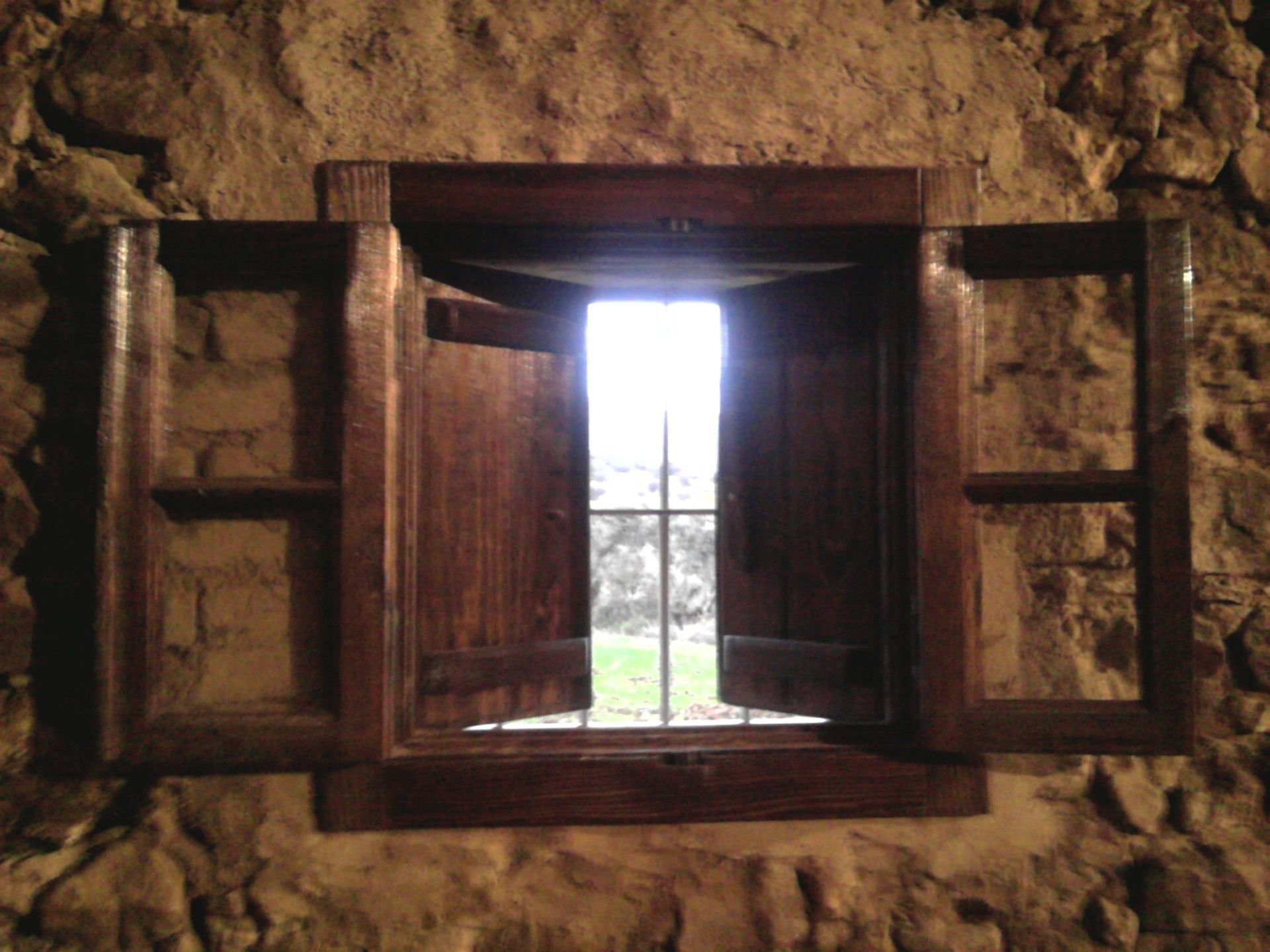 Una ventana de madera con contraventanas abiertas en una pared de piedra.