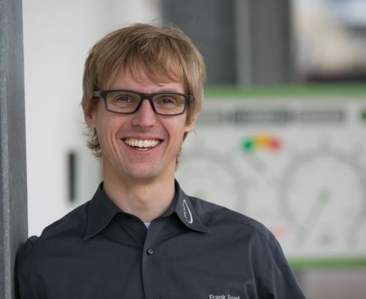 Ein Mann mit Brille und schwarzem Hemd lächelt