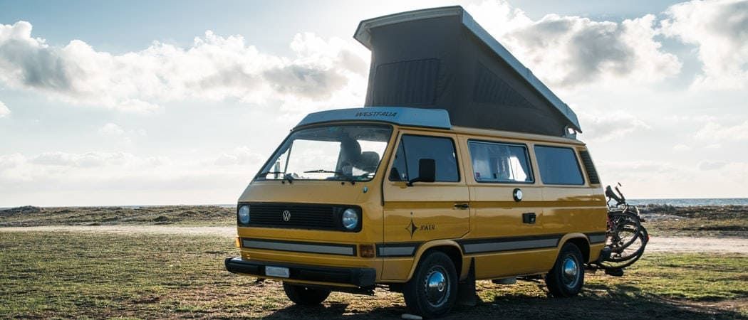 Ein gelber VW Caravan mit Aufstelldach steht auf einem Feld.