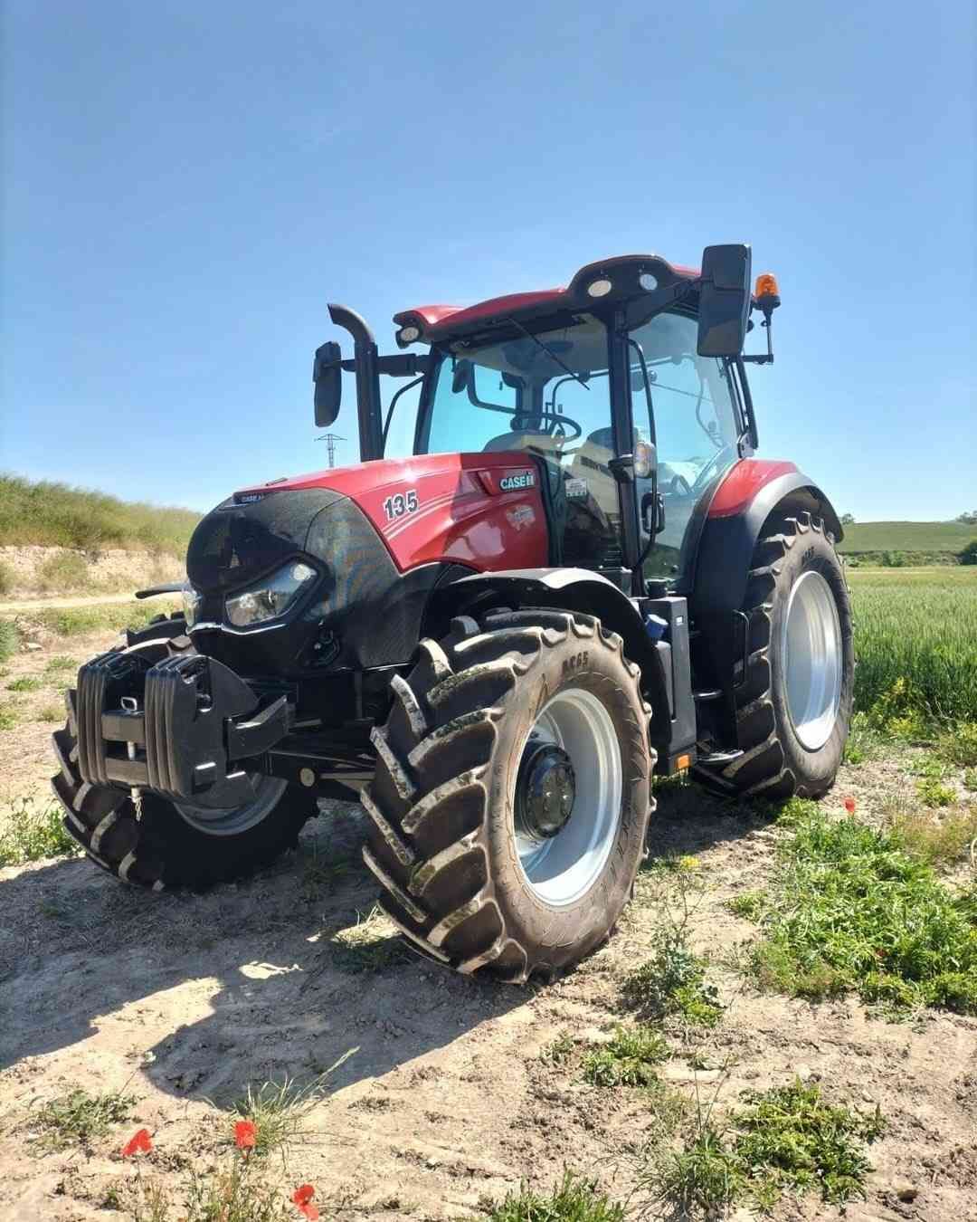 Tractor Case IH rojo en un campo de hierba bajo un cielo azul claro.