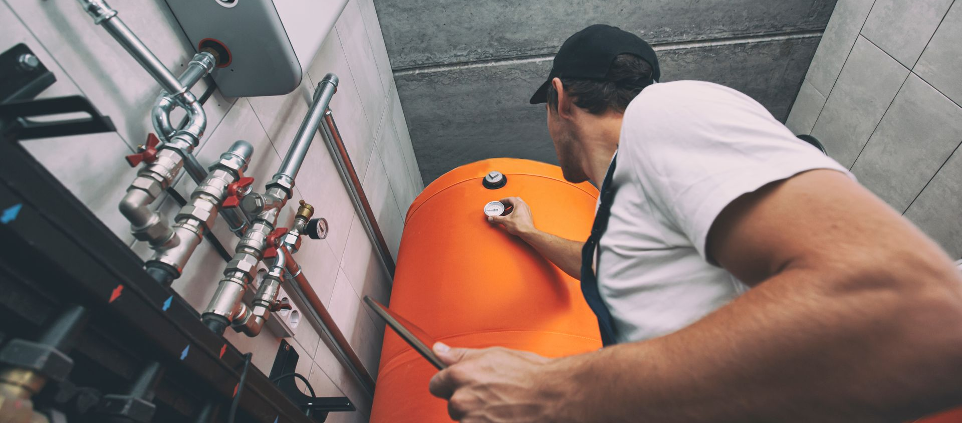 Un monsieur tenant un outil devant une chaudière de couleur orange
