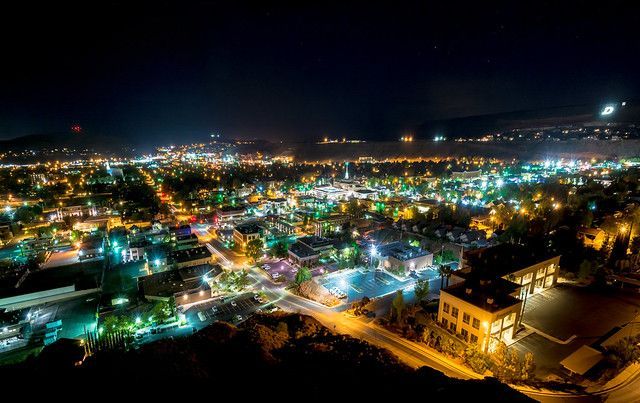 Nighttime panoramic cityscape with colorful lights and a dark hillside in the foreground