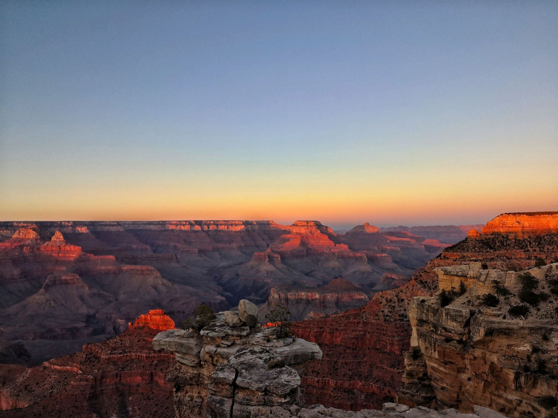 Sunset over the Grand Canyon with layered red cliffs and a pale blue sky