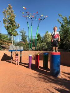 Child standing on colorful playground stepping posts with a pig sculpture and flower-shaped poles nearby