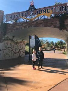 Two people standing under the Thunder Junction archway in a sunny park.