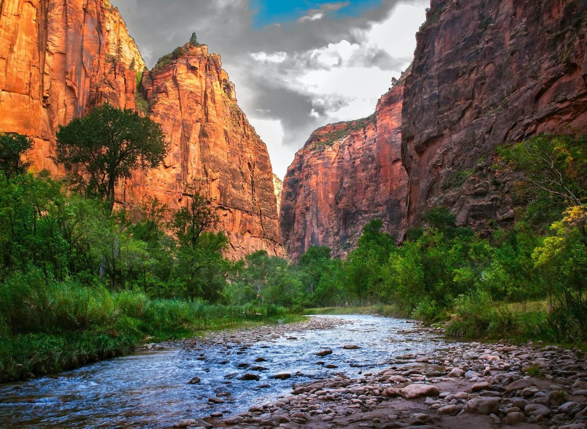 Canyon walls glowing at sunset above a rocky river with green vegetation