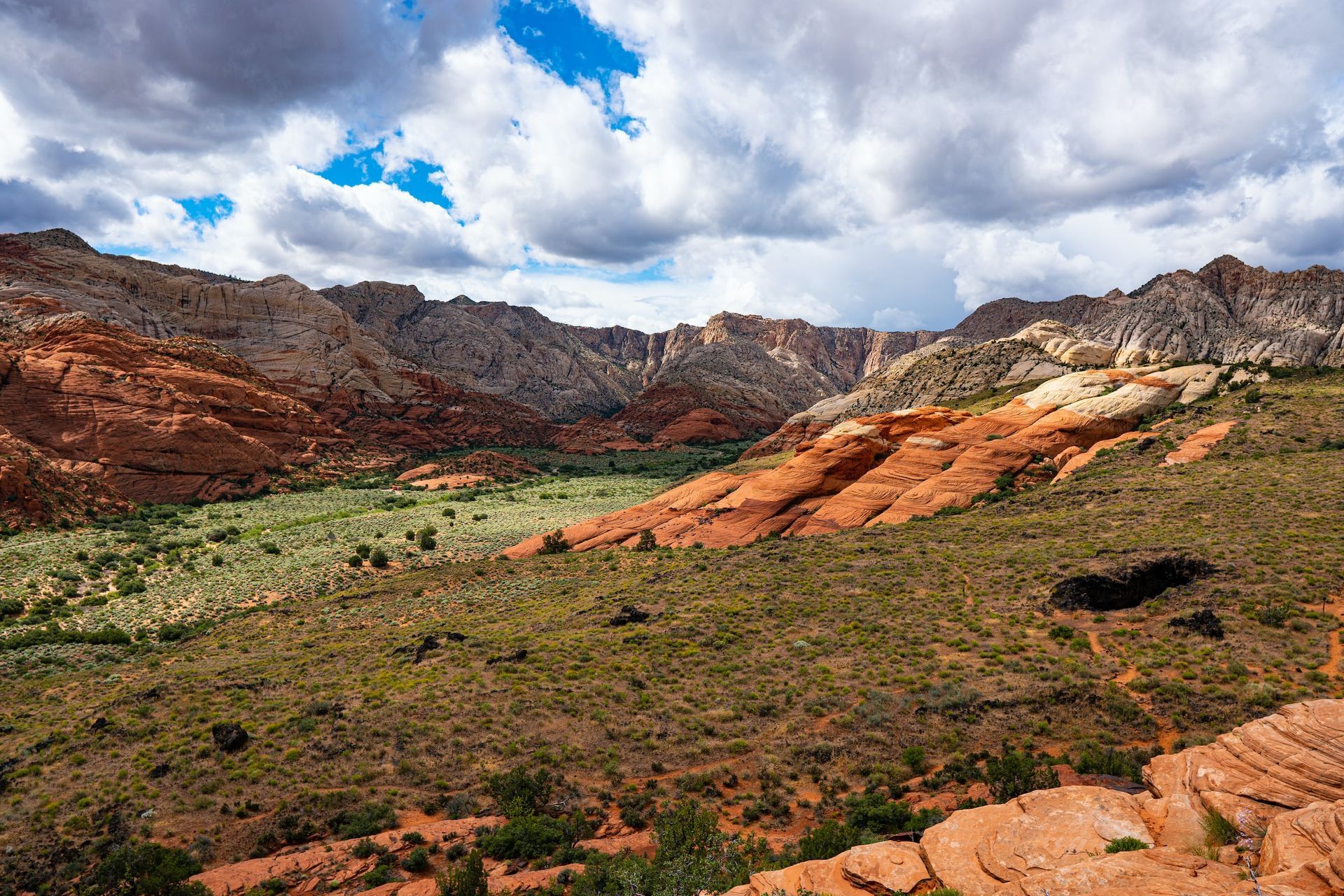 Red rock canyon with green valley and cloudy blue sky