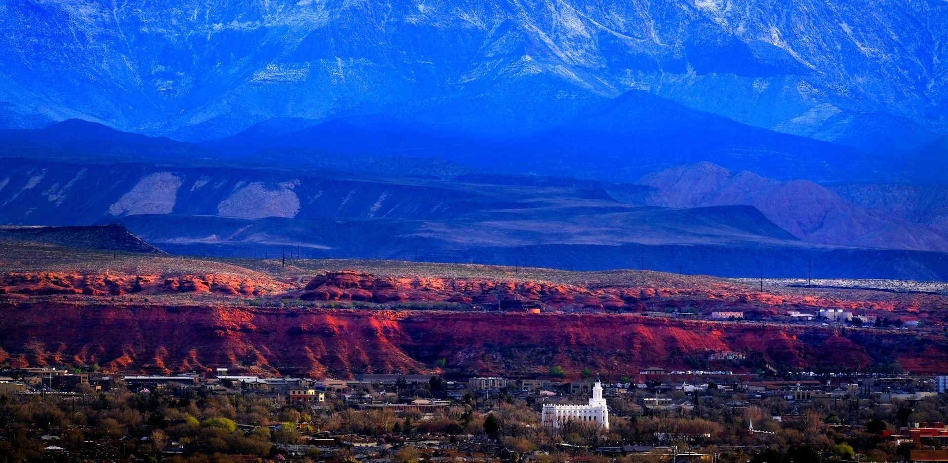 Wide cityscape under blue mountains with a vivid red sunset glow in the foreground
