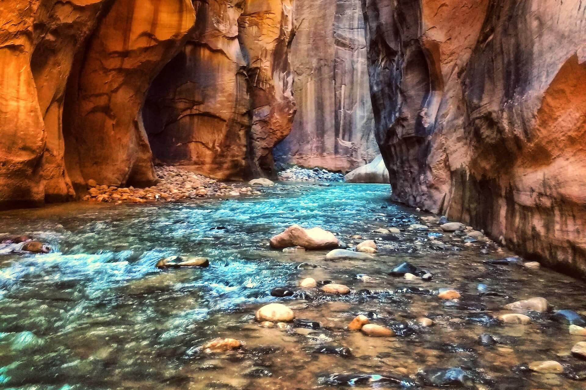 Rocky canyon stream with clear turquoise water and sunlit orange cliffs