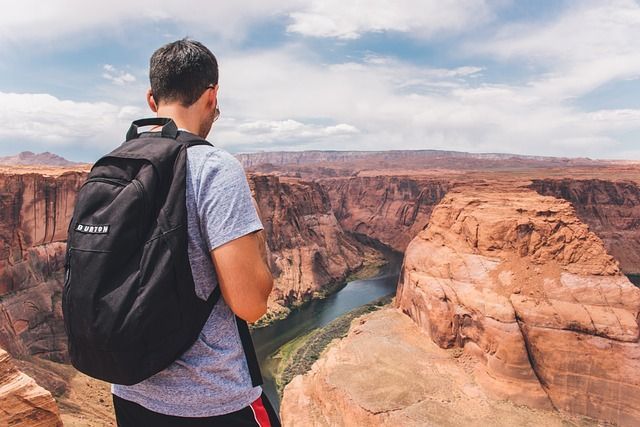Person with backpack overlooking a canyon and river from a rocky cliff.