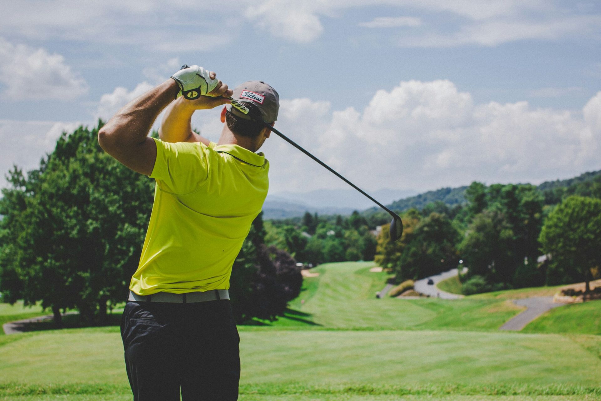 Golfer in neon green shirt following through on a swing on a sunny golf course