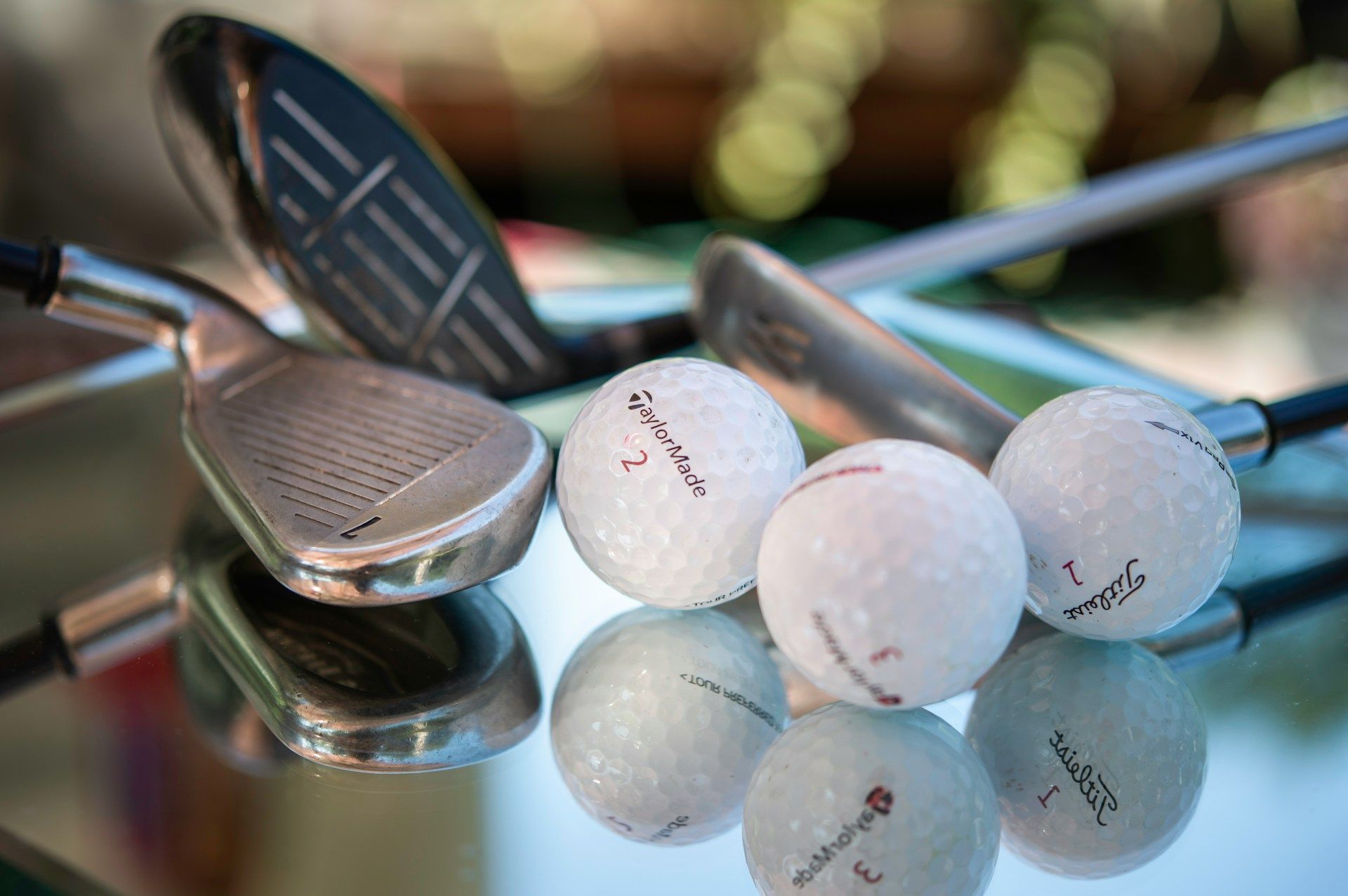 Golf clubs and white golf balls resting on a reflective glass surface.