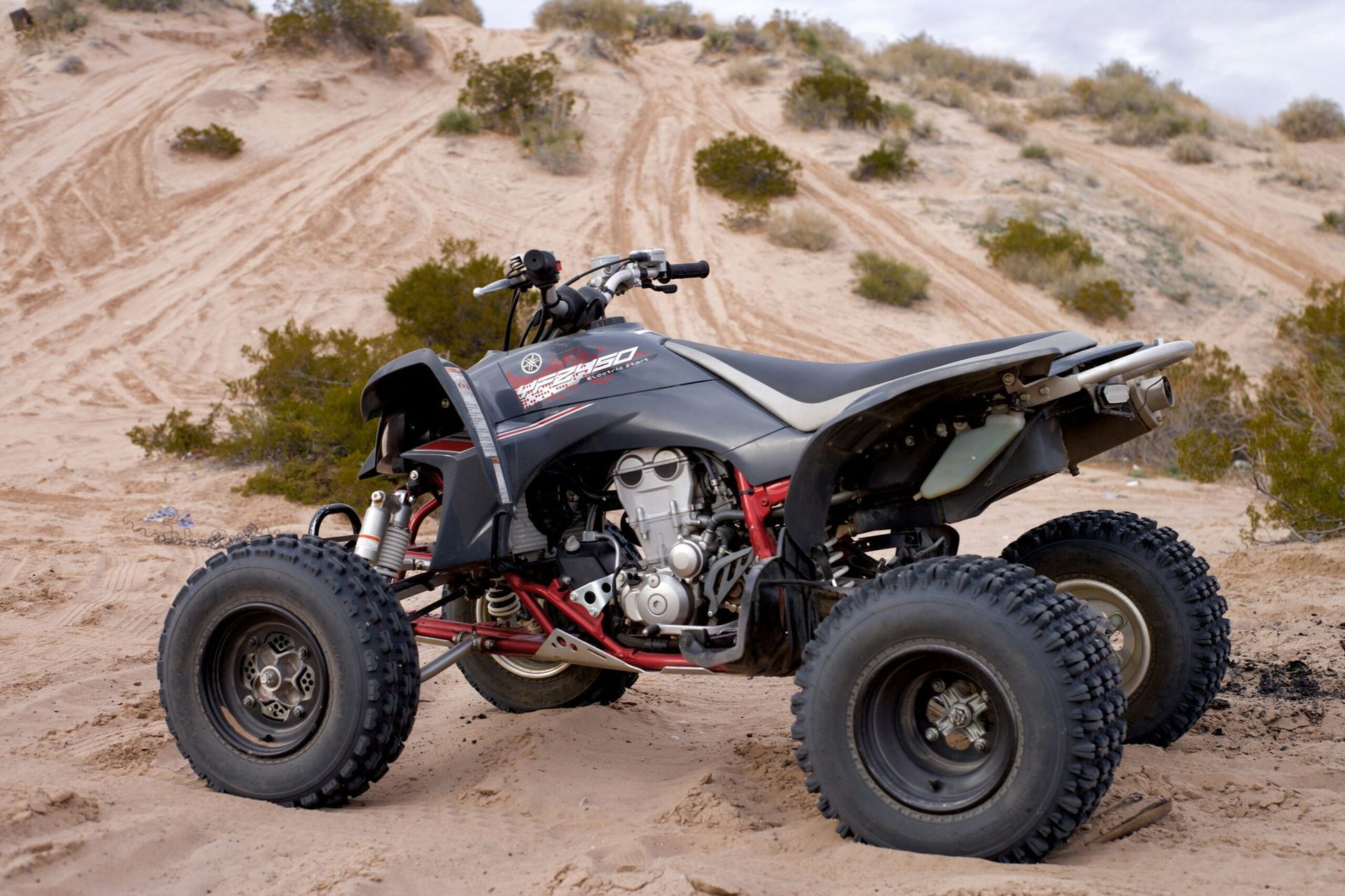 Black all-terrain quad bike parked on sandy dunes with sparse desert shrubs
