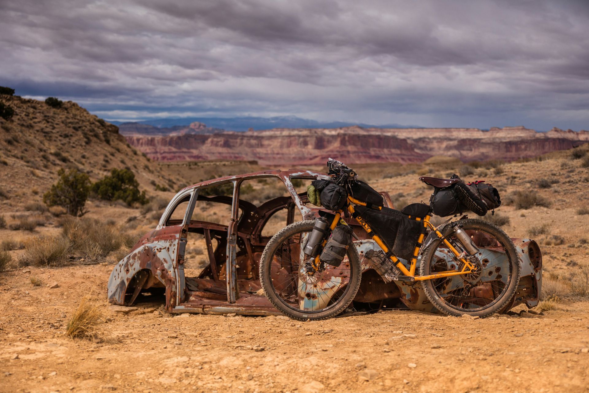 Two mountain bikes beside a rusted car shell in a desert canyon landscape