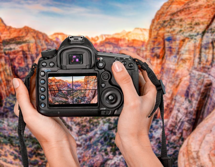 Hands holding a DSLR camera, framing a canyon landscape at sunset