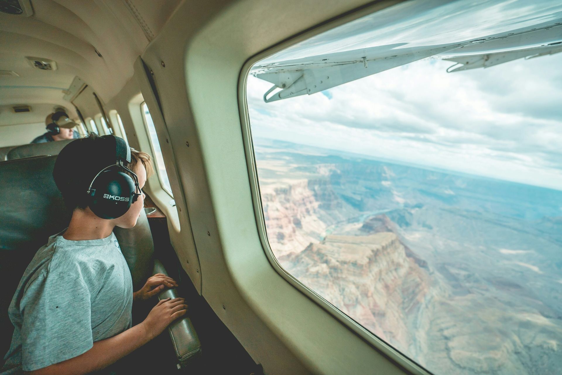 Passenger in headset looks out airplane window at desert landscape and wing view