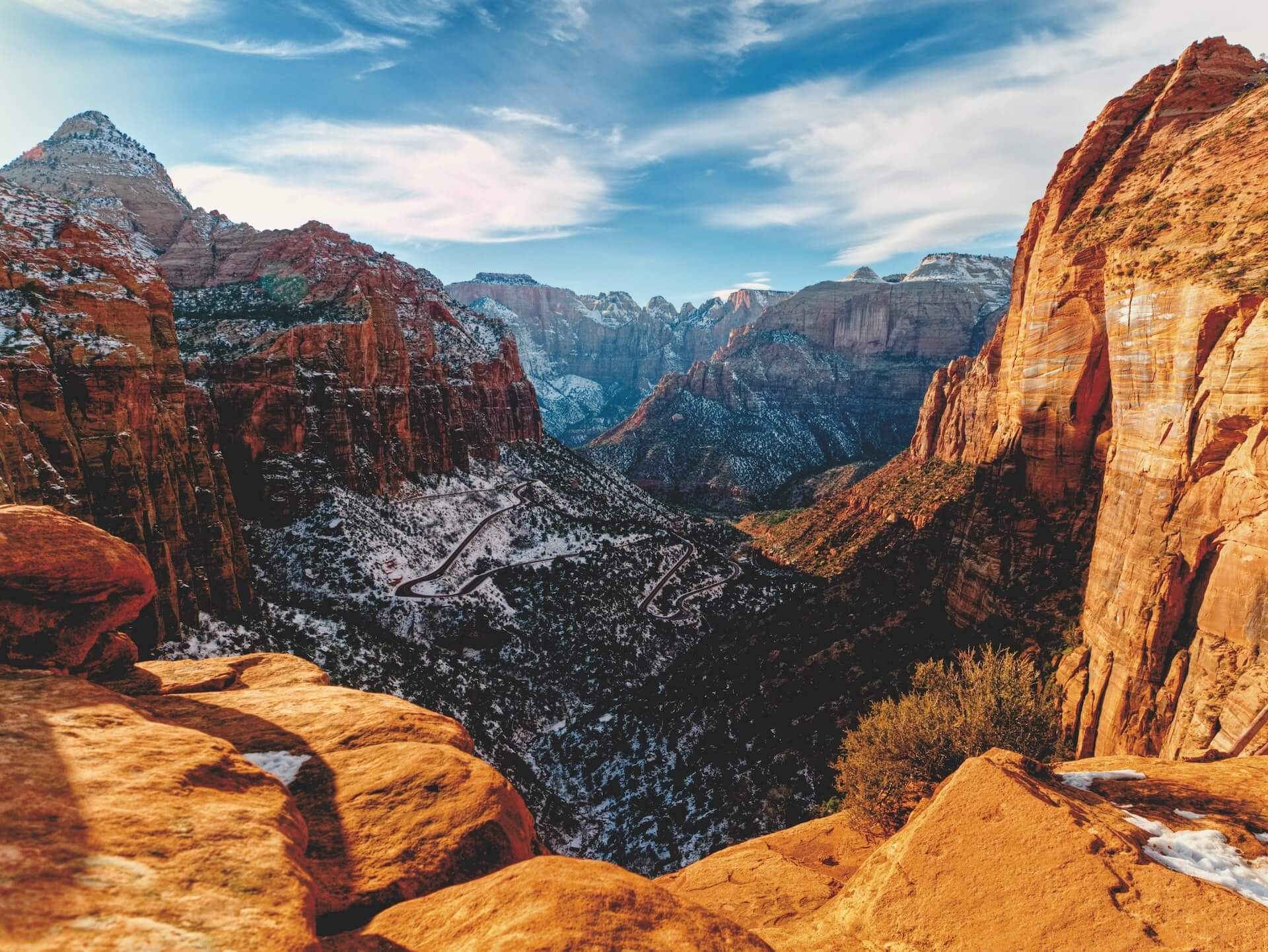 Snow-dusted red rock canyon with sunlit cliffs and a winding valley under a blue sky