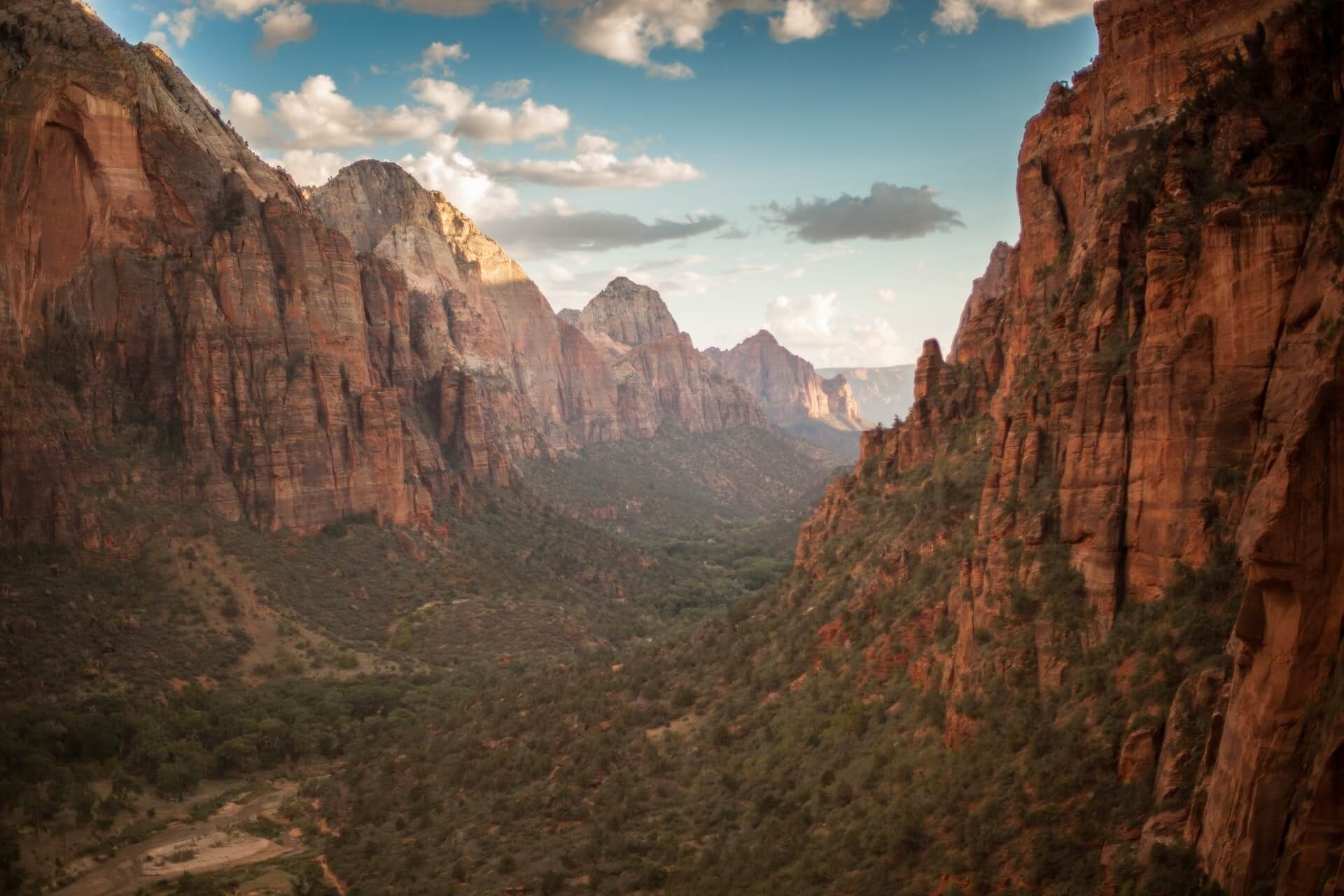 Red sandstone canyon with towering cliffs and a green valley under a cloudy blue sky