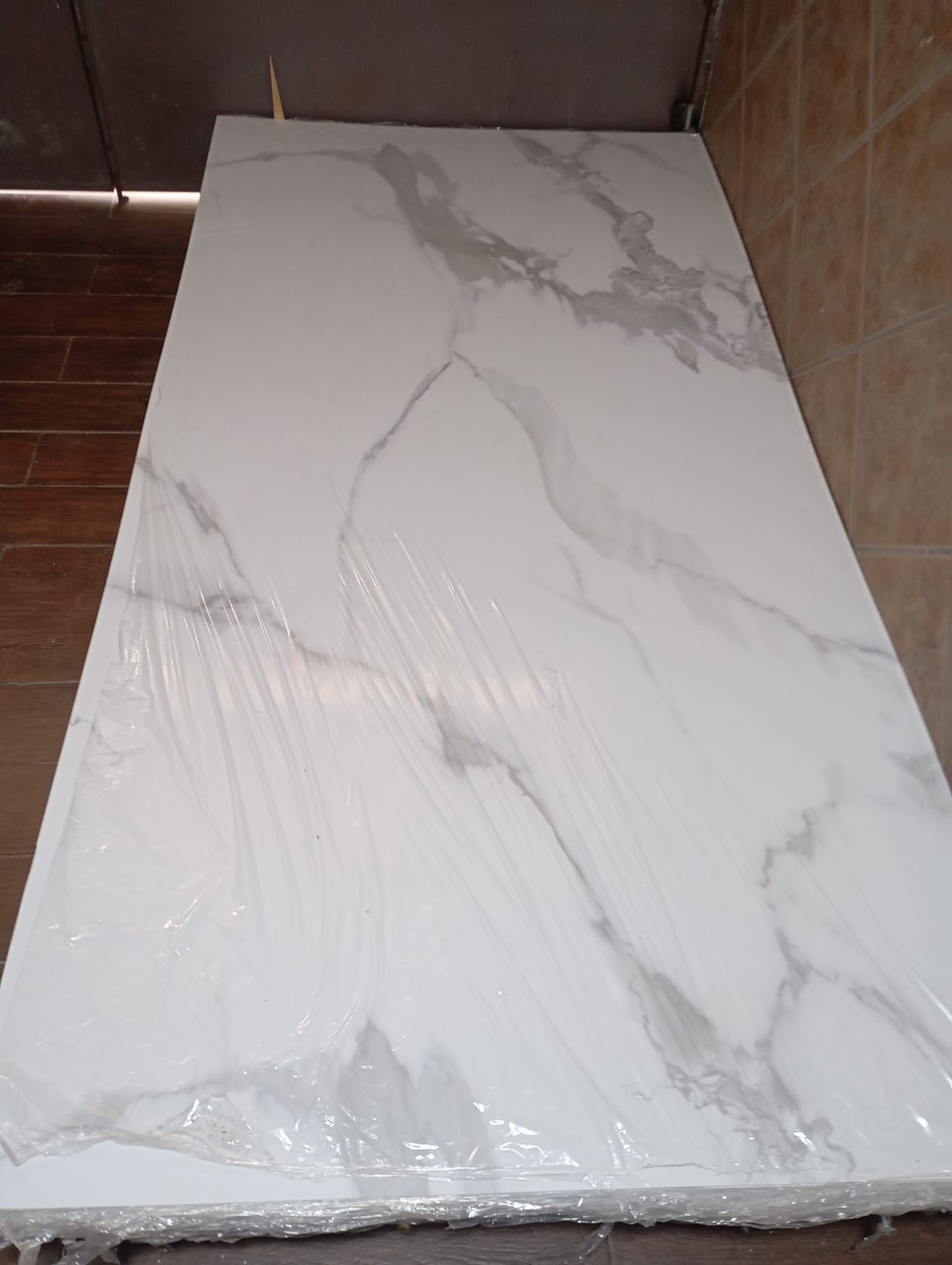 Una encimera de mármol blanco está envuelta en plástico y colocada sobre un suelo de madera.