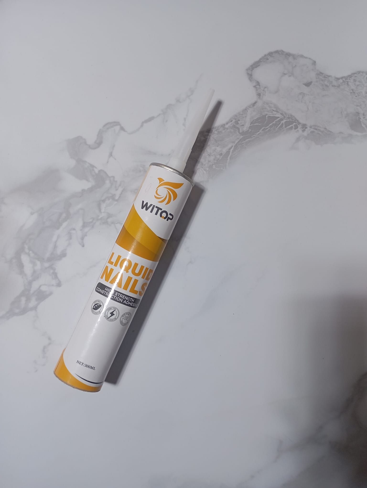 Una botella de adhesivo líquido para paredes reposa sobre una superficie blanca.