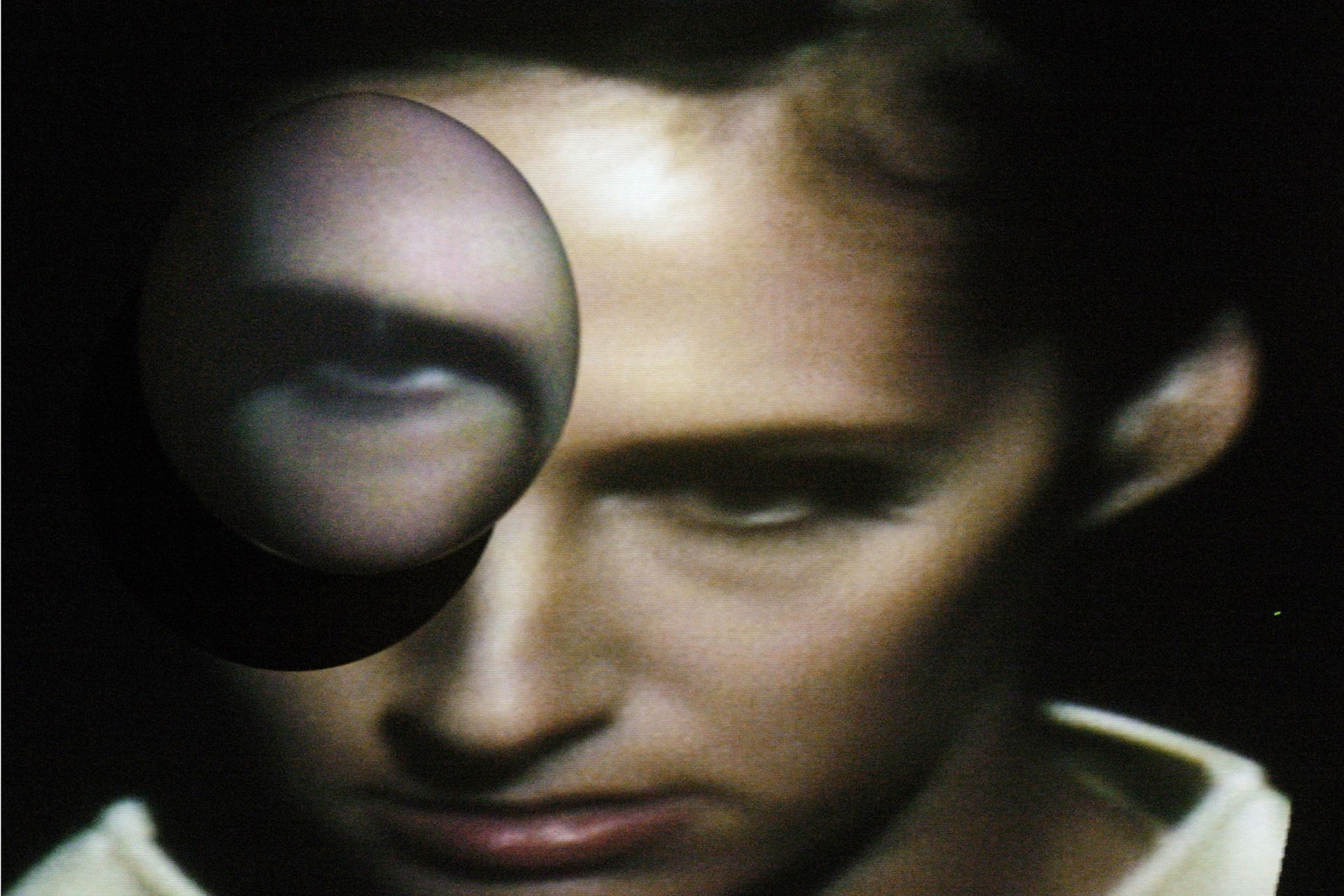 Un rostro en sombra parcial con un reflejo esférico y flotante de un ojo.