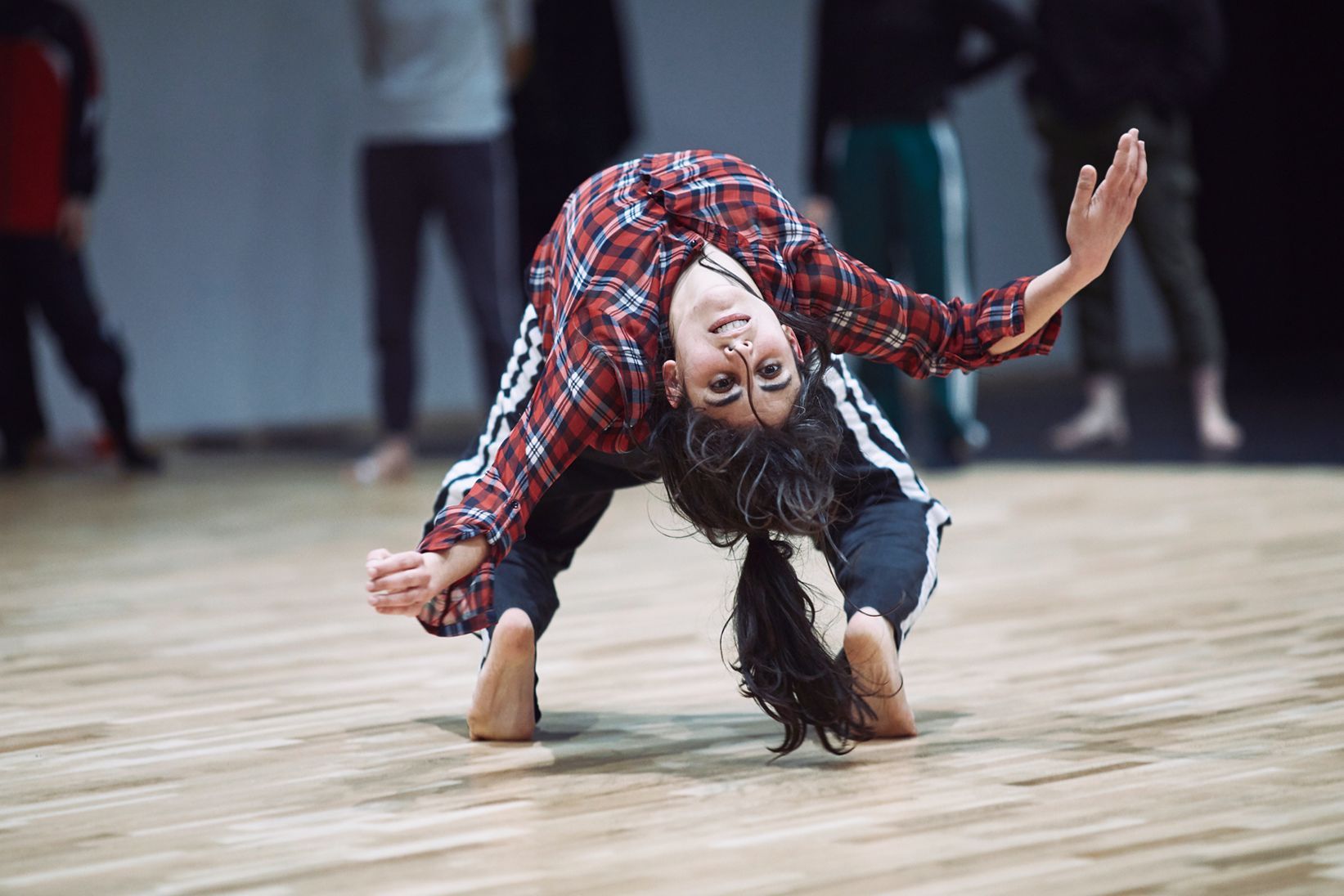 Mujer con camisa a cuadros se inclina hacia atrás, con las manos en los pies, en el estudio de baile.