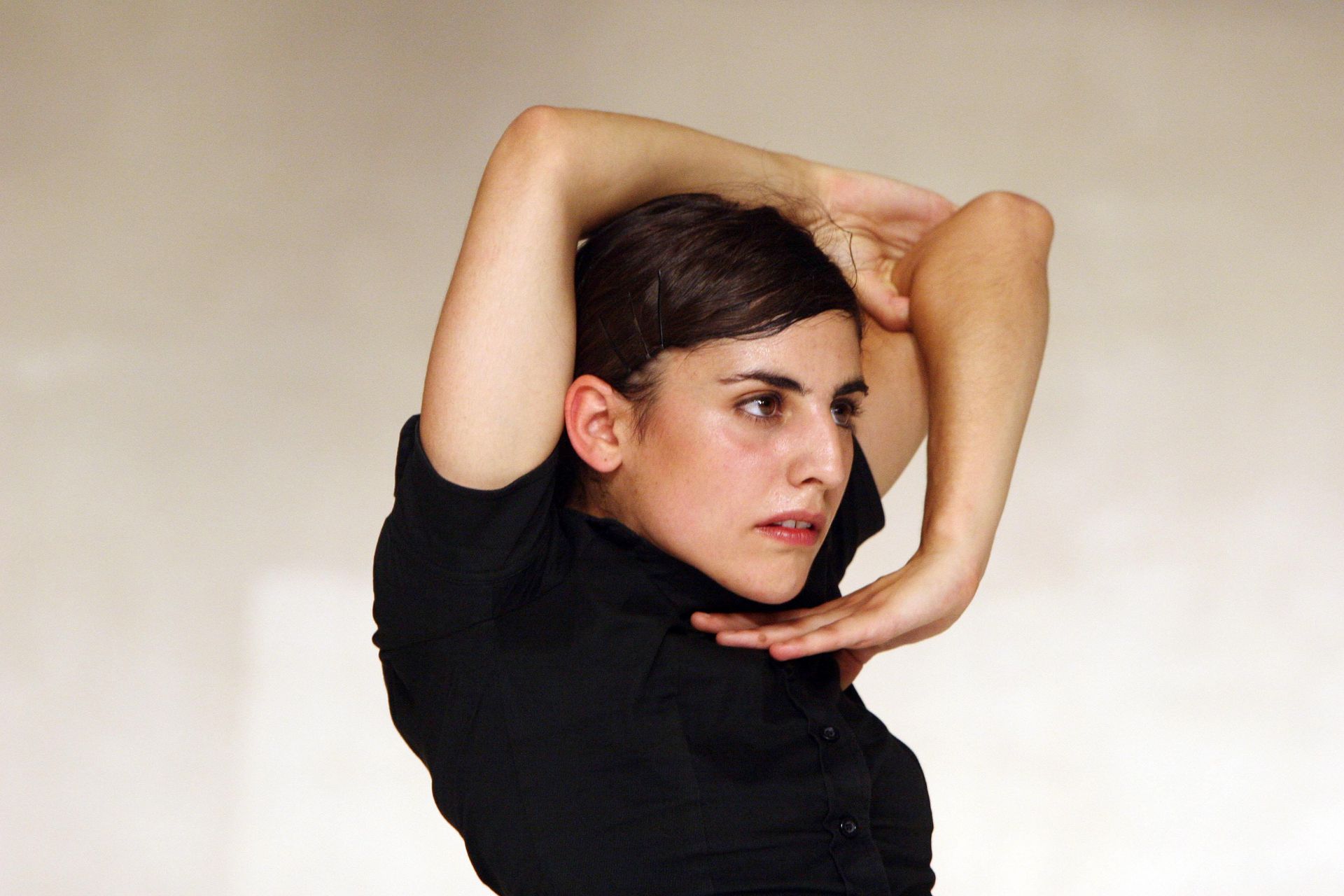 Mujer con camisa negra arquea la espalda, brazos levantados e inclinados, cabeza girada y expresión concentrada.