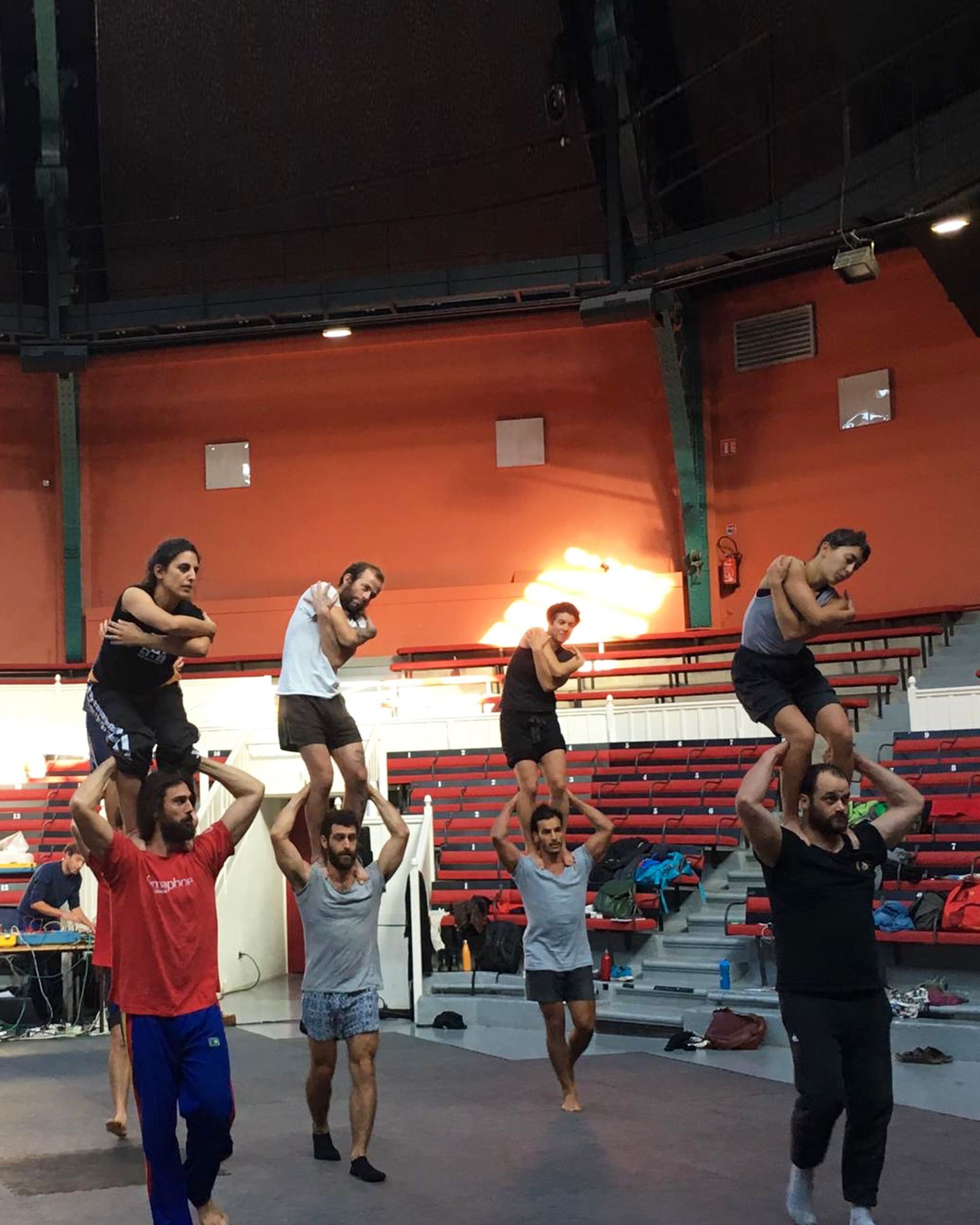 Hombres realizando una pirámide humana en un espacio cerrado. La fila superior con los brazos en alto