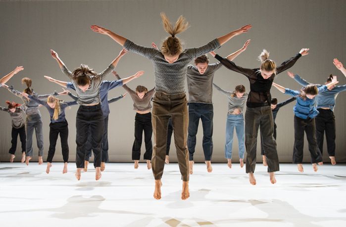 Bailarines vestidos con ropa informal saltando en el aire con los brazos extendidos contra un fondo claro.