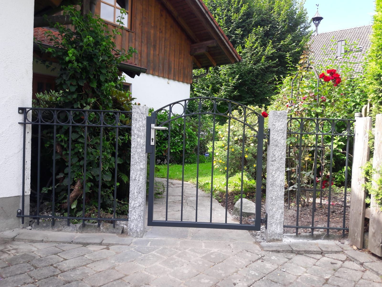 Schmiedeeisentor mit Granitpfosten und Garten dahinter