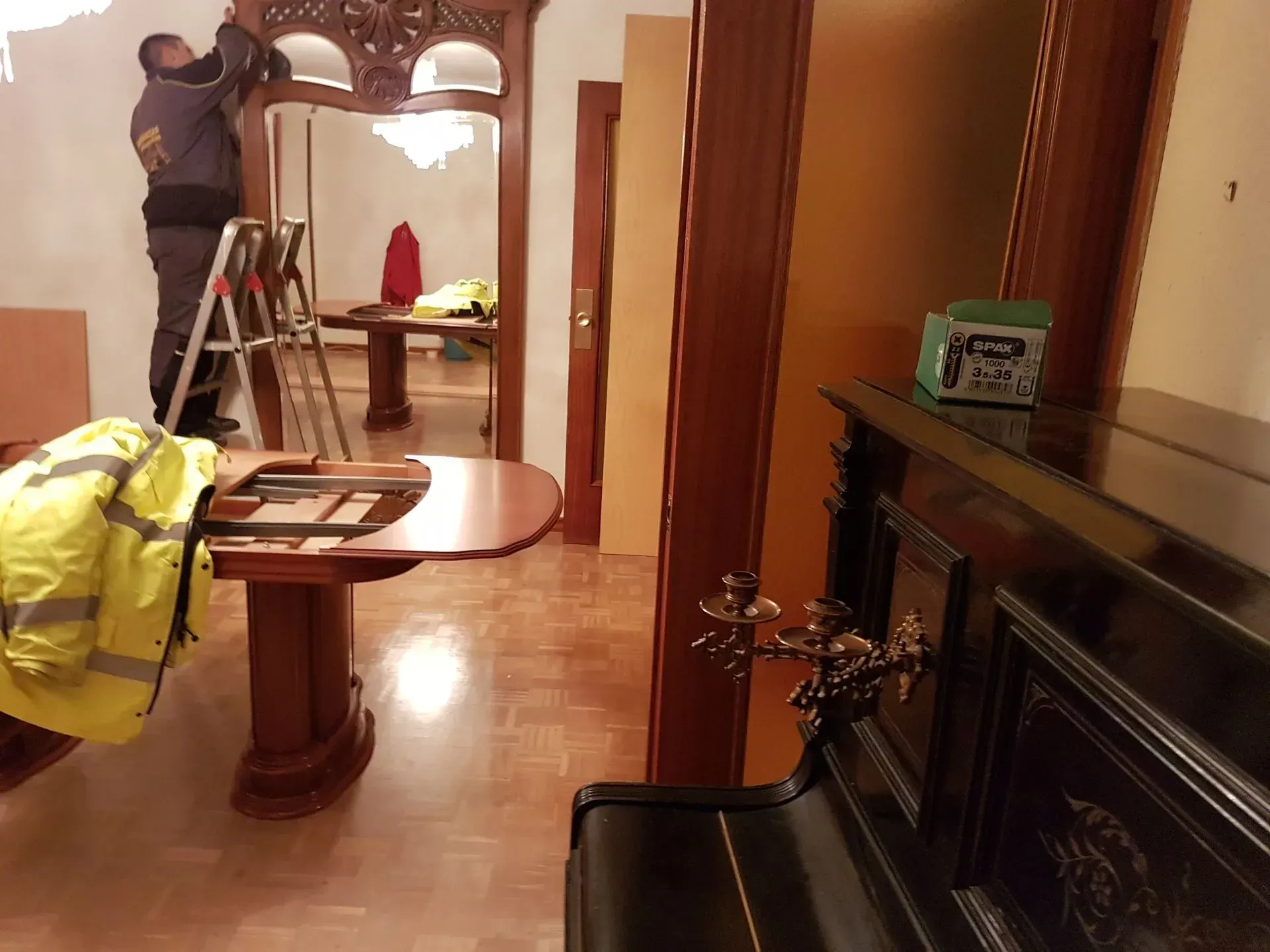 Hombre subido a una escalera instalando molduras decorativas de madera sobre una puerta. Fotografía de interior.