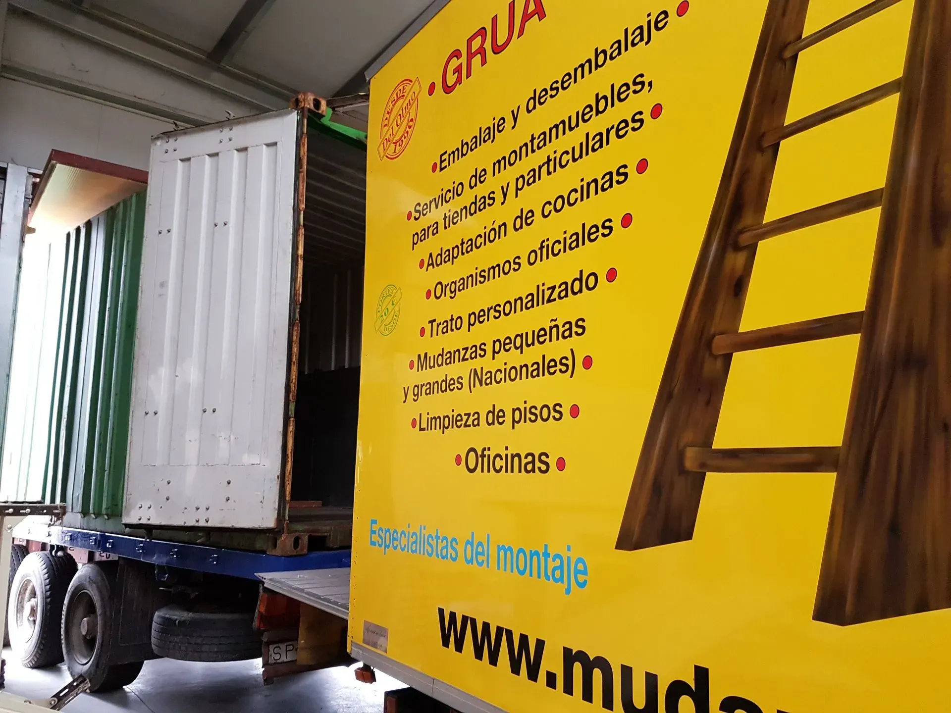 Un camión con un contenedor, junto a un cartel amarillo que anuncia servicios de mudanza, con una escalera en la imagen.