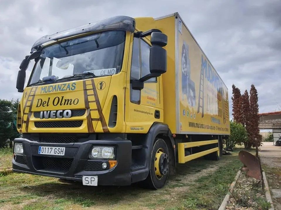 Camión de mudanzas amarillo estacionado en el césped; se ven los letreros 