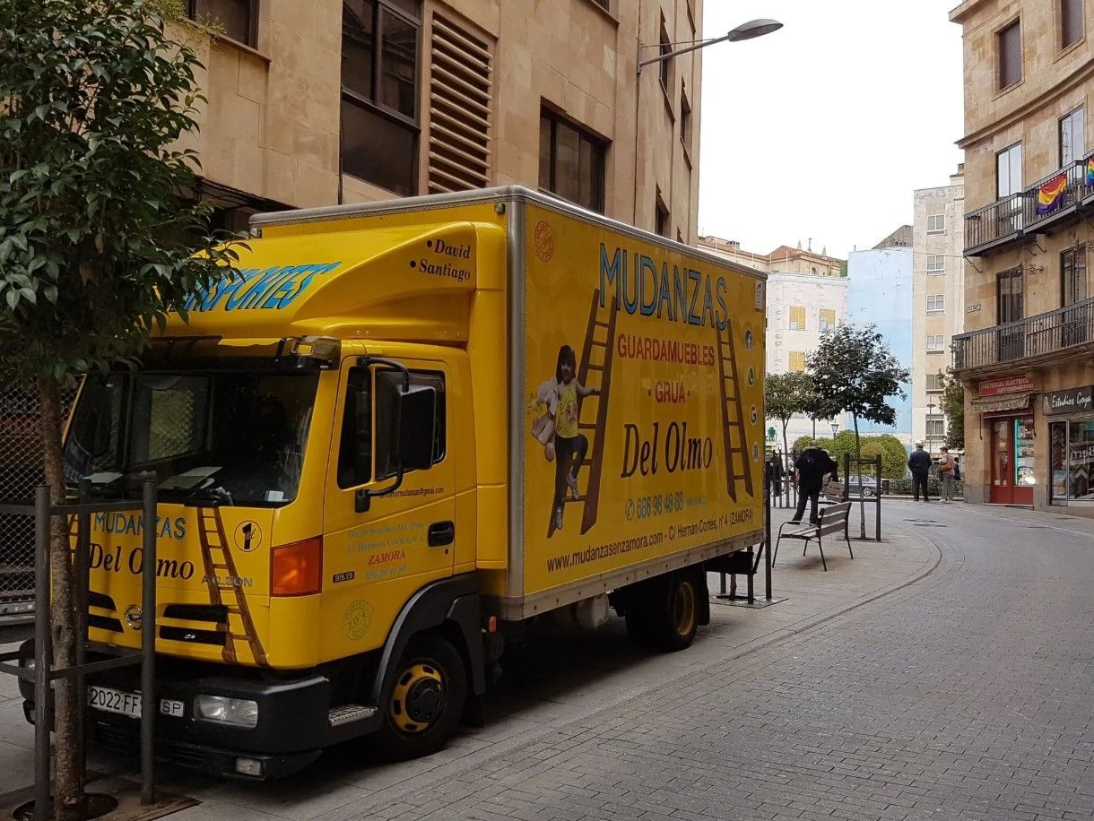Camión de mudanzas amarillo estacionado en una calle adoquinada de una ciudad.