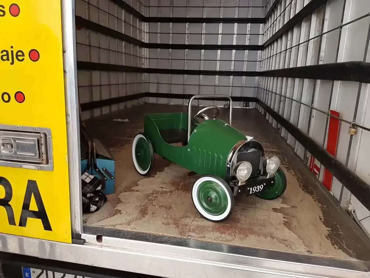 Coche de pedales verde dentro de un vehículo, cerca de un panel amarillo.