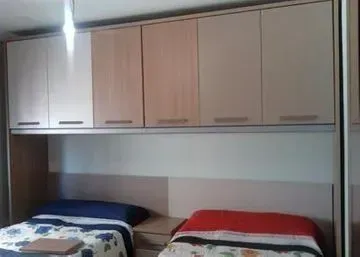 Dormitorio con dos camas, armarios superiores color beige, una cama azul y blanca, la otra roja.