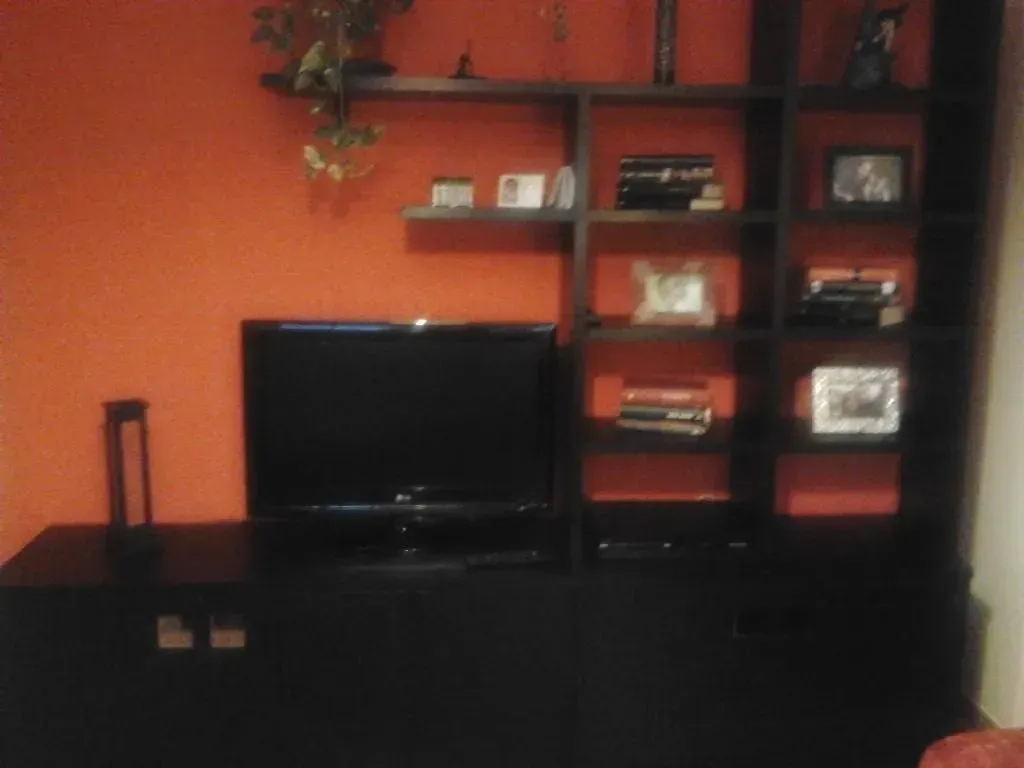 Mueble de entretenimiento negro con televisor, estantes y pared naranja.