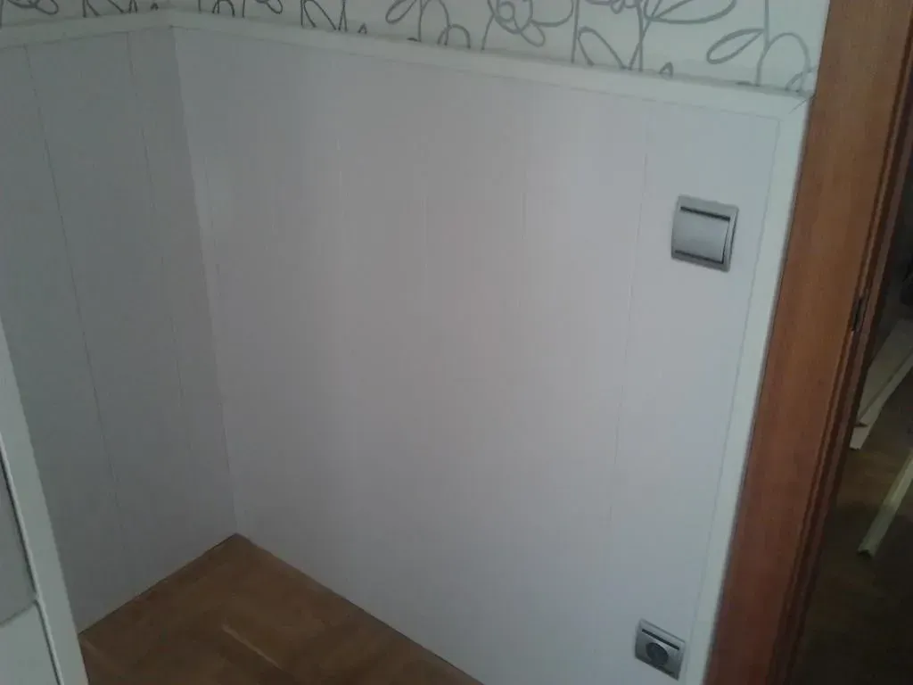 Esquina de pared con paneles blancos e interruptores de luz. Plataforma de madera en primer plano.