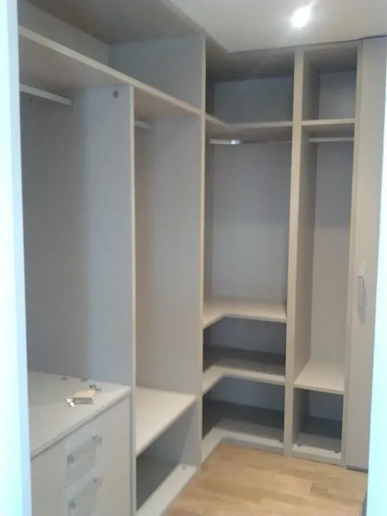 Armario empotrado vacío con estantes y barras para colgar ropa. Beige claro, suelo de madera.