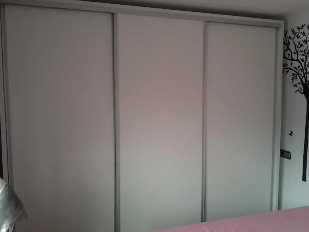 Armario de tres puertas correderas con paneles blancos y detalles plateados. A la derecha hay una pegatina negra de un árbol.